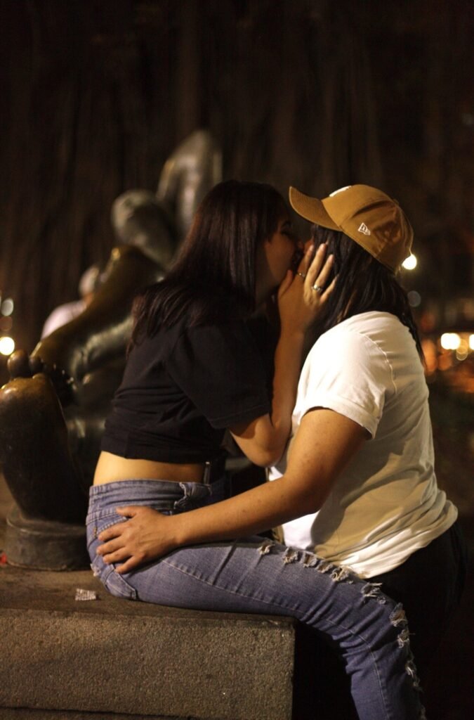 Duas pessoas se beijam sentadas junto a uma escultura no Largo do Arouche, à noite