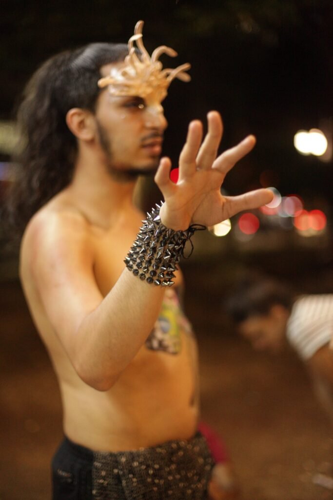 O mesmo performer, de máscara esculpida e bracelete de spikes, gesticula no Largo do Arouche
