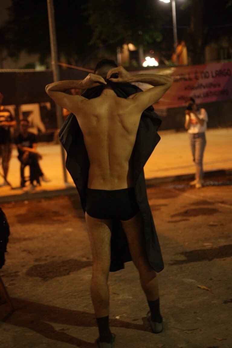 plexoisaac, de costas, abre a capa preta no Largo do Arouche, à noite