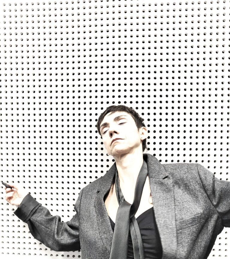 Retrato em preto e branco de Christina Elias, de paletó, diante de uma parede perfurada