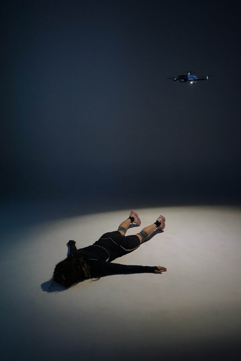 Carmen Ixchel Maya deitada sob um foco de luz, com um drone suspenso acima, em PAS DE DEUX