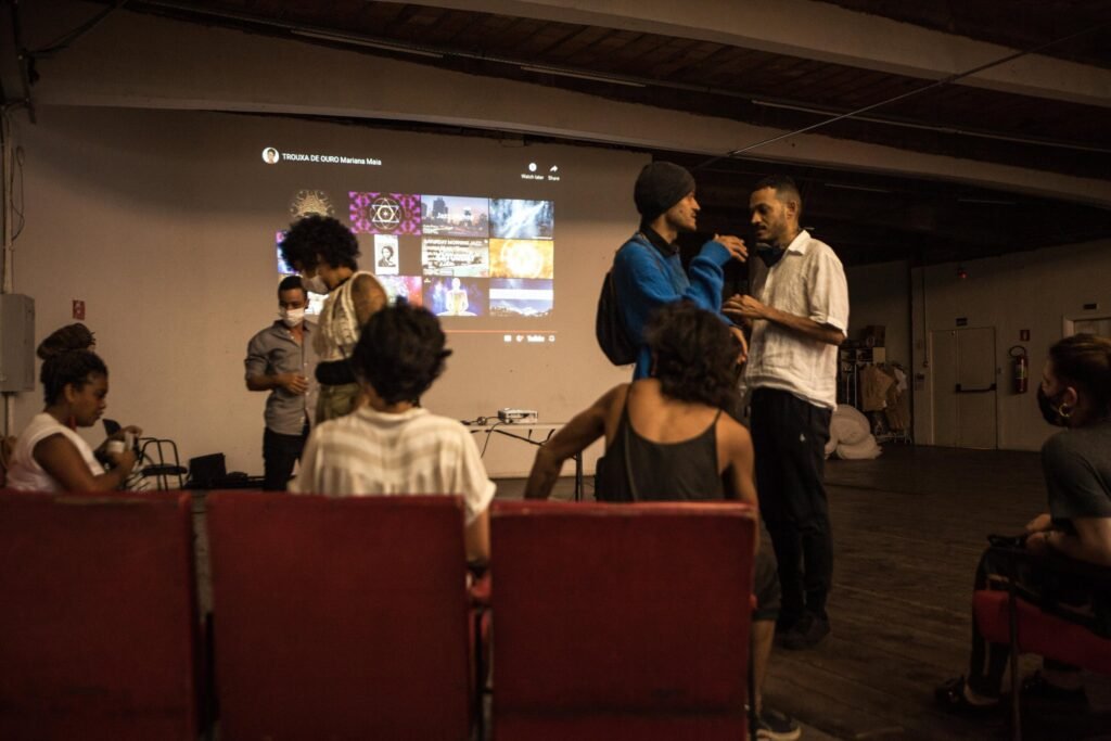 Público e artistas diante da tela de projeção na festa de abertura, na Casa do Povo