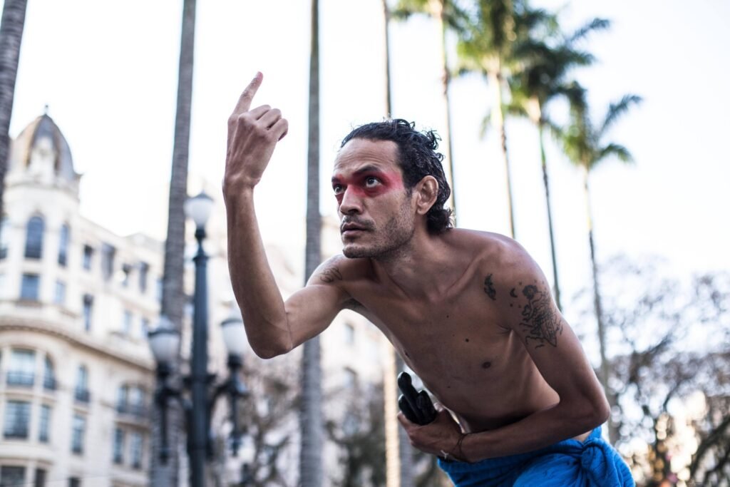 Ismael Trabuco, de olhos pintados de vermelho, aponta para o alto entre as palmeiras da Praça da Sé