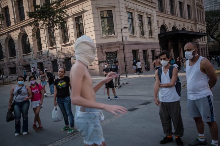 Reyan Perovano, com a cabeça coberta por atadura, diante do público numa praça do centro de São Paulo