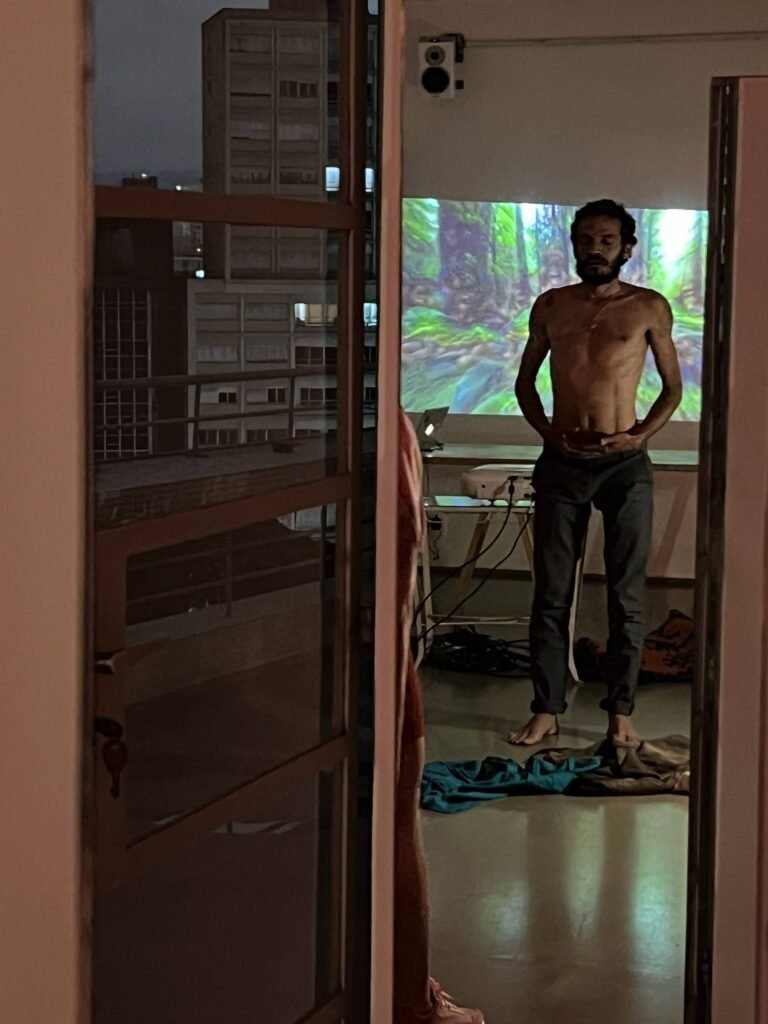 Ismael Trabuco de pé diante de uma projeção de floresta, visto através de uma porta