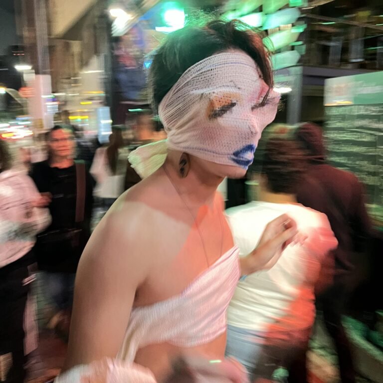 Reyan Perovano, com a máscara de atadura pintada com olhos e lábios azuis, em meio ao movimento da rua