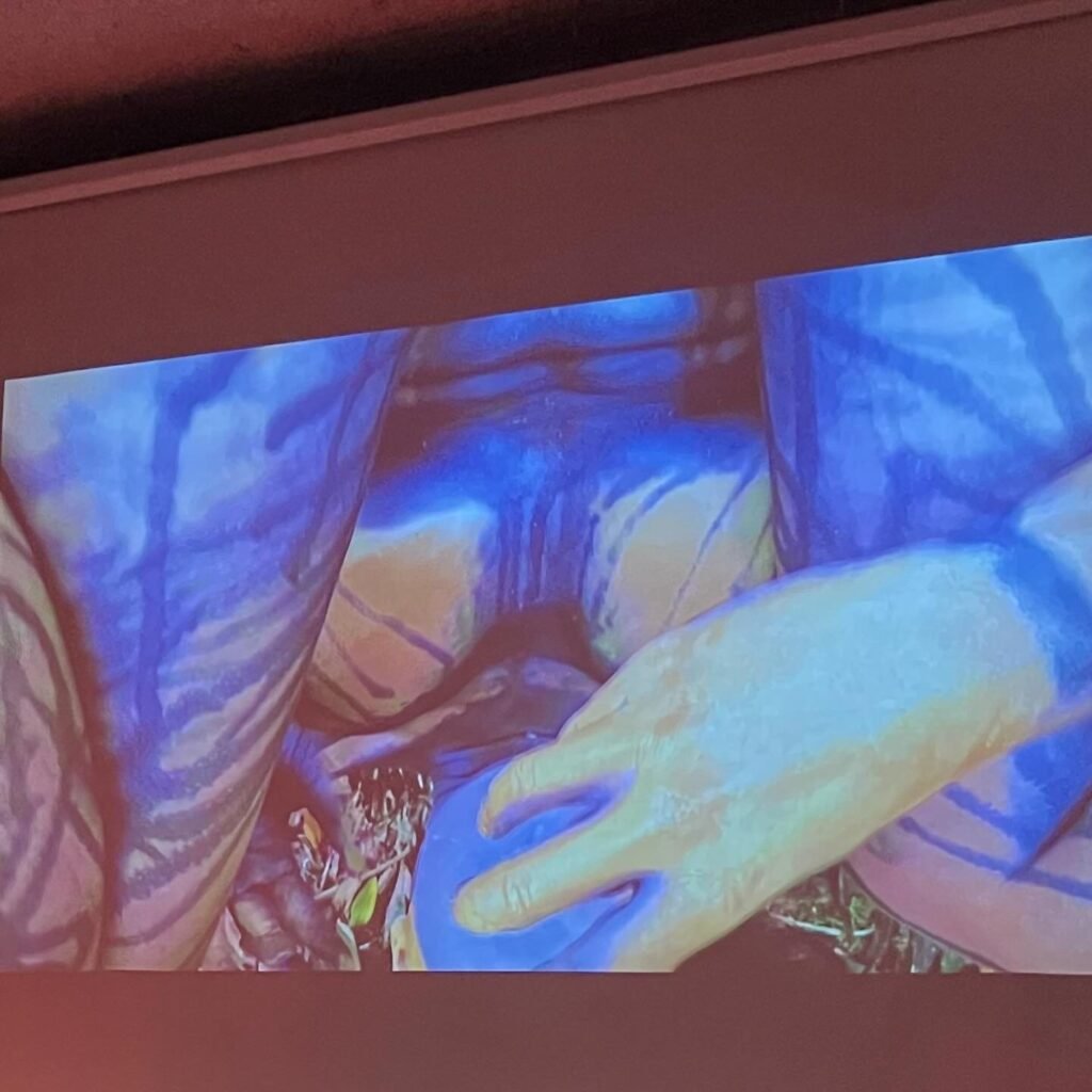 Videoperformance projetada no auditório da Ação Educativa na noite de abertura: mão sobre um corpo coberto de manchas azuis