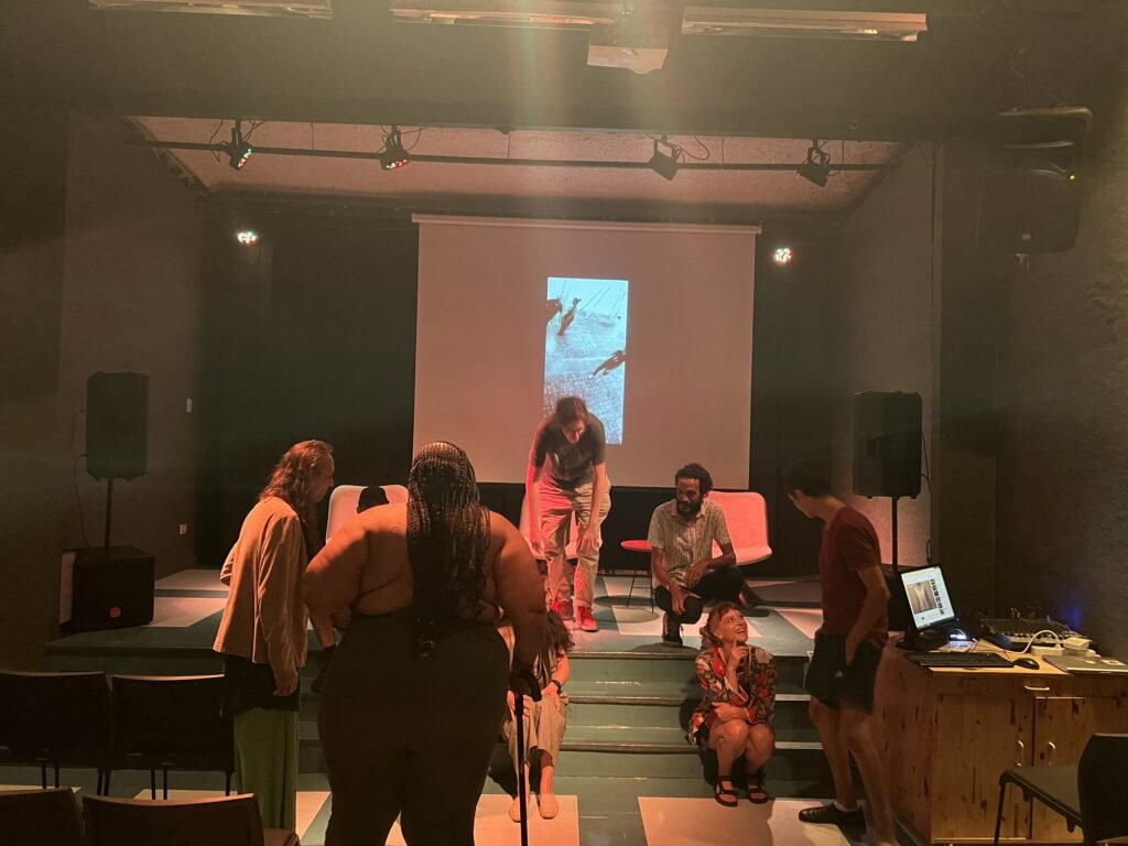Artistas e público confraternizam diante da tela no auditório da Ação Educativa, no fim da noite de abertura