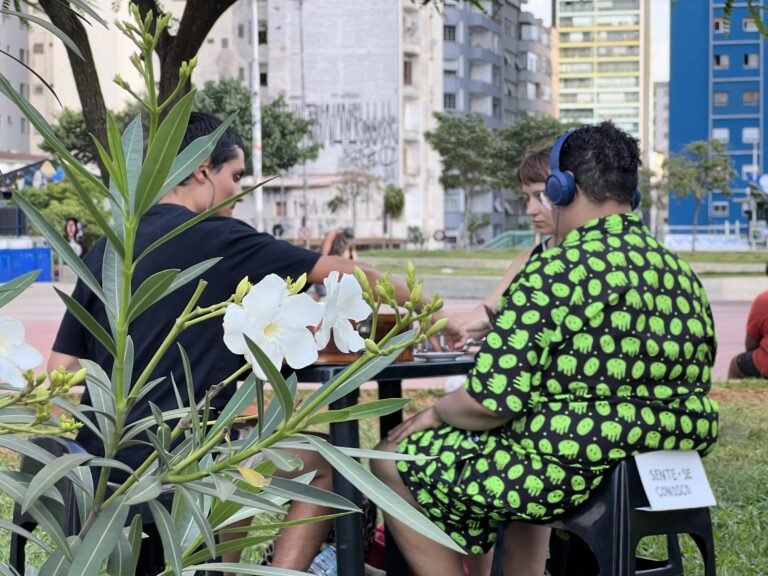 Pessoa de fones de ouvido e camisa estampada sentada à mesa da dupla, entre flores, na Praça Roosevelt