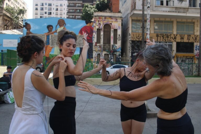 Quatro performers ligadas pelo fio diante dos murais e dos casarões da Praça Roosevelt