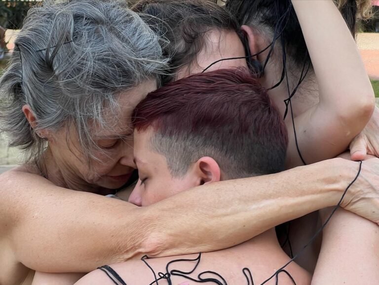 Close de um abraço entre performers, com o fio preto sobre a pele