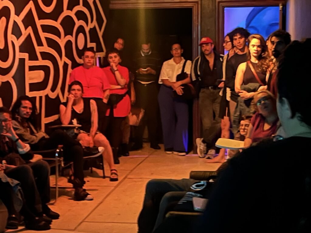 Público sentado e de pé na sala de paredes grafitadas do Estúdio Lâmina, durante a exibição