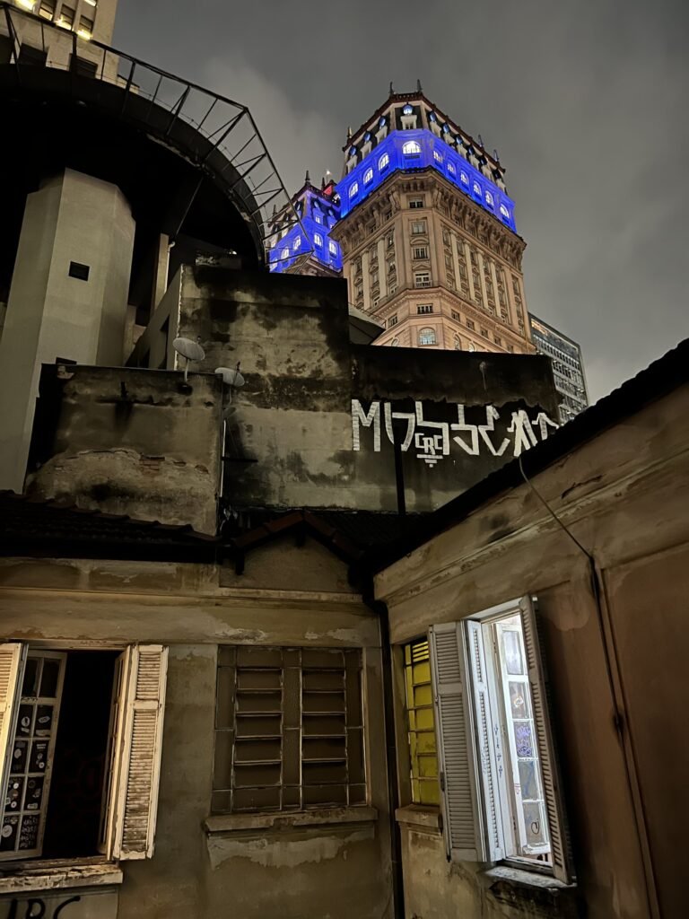 Vista noturna dos fundos do prédio do Estúdio Lâmina, com o Edifício Martinelli iluminado ao fundo
