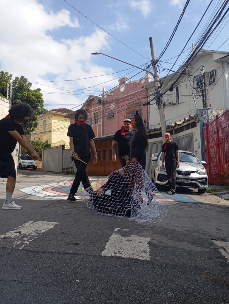 Participantes do workshop numa rua do Bixiga, em volta de uma pessoa coberta por uma rede