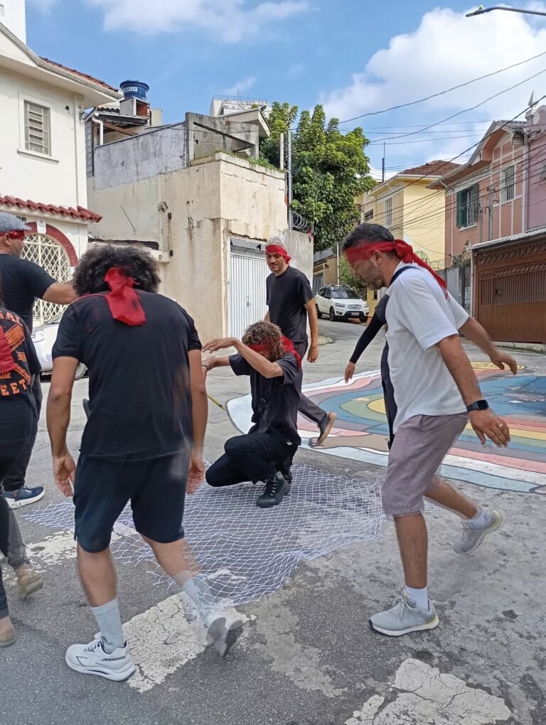 Participantes de olhos vendados giram em roda sobre o asfalto pintado de uma rua do Bixiga