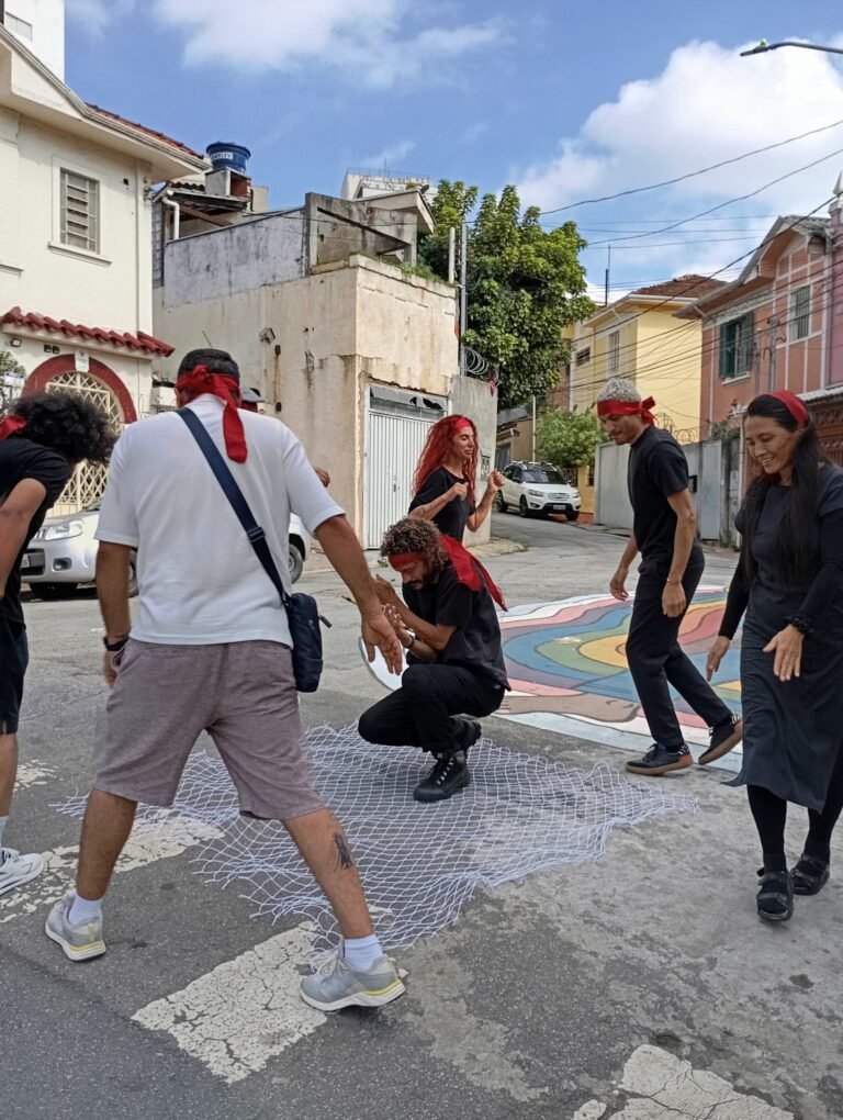 Participantes de olhos vendados em roda numa rua do Bixiga, com a pessoa da rede ao centro