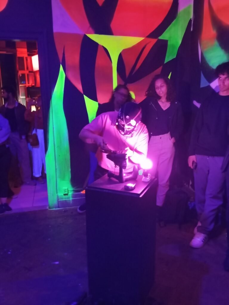 Integrante da Boleia Coletiva de balaclava trabalha numa sola sobre um pedestal, sob luz rosa