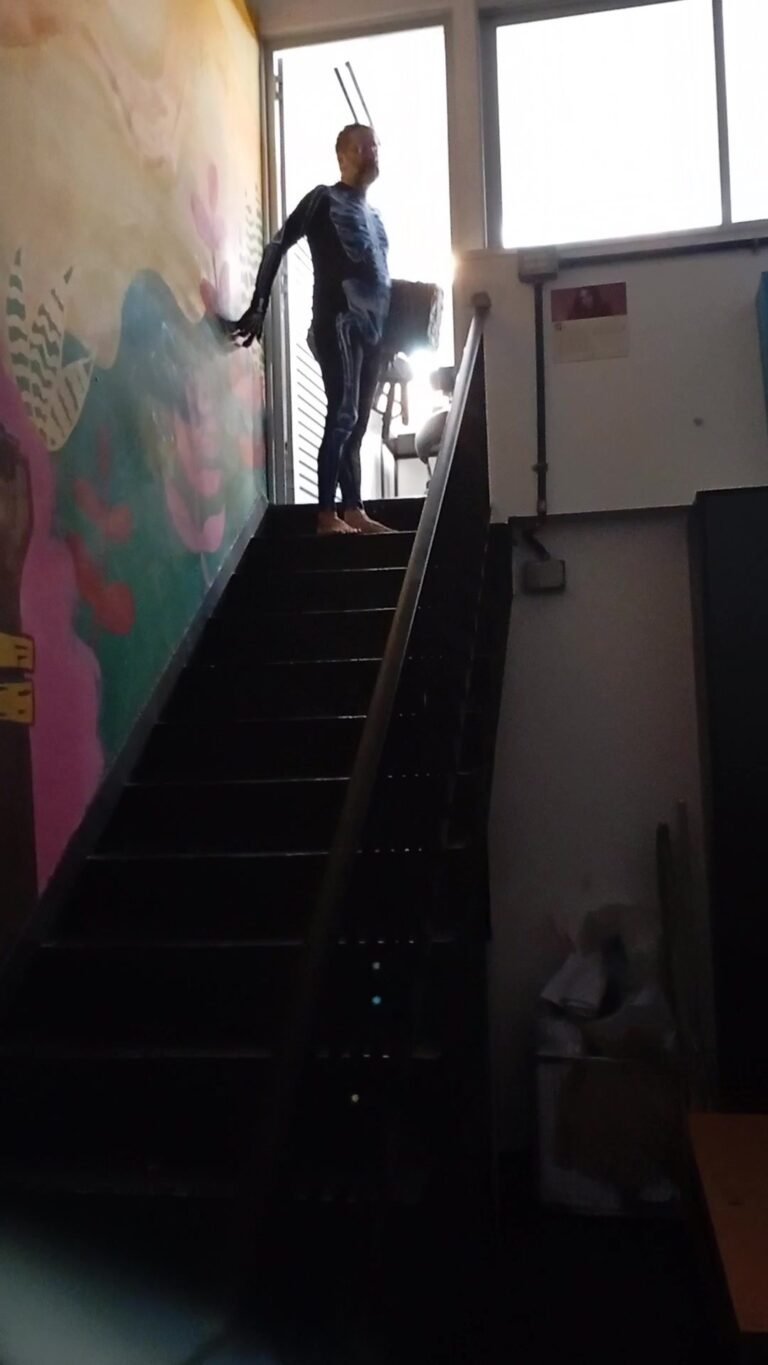 Figura de macacão no alto da escada, junto à porta iluminada, prestes a sair de cena