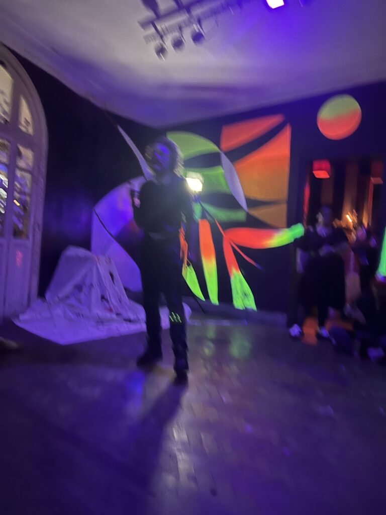IsTo no salão do Estúdio Lâmina sob luz roxa, com o público em volta e o mural colorido ao fundo