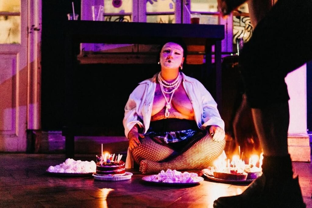 Marília Hermes sentada no chão entre bolos com velas acesas e pratos de suspiros