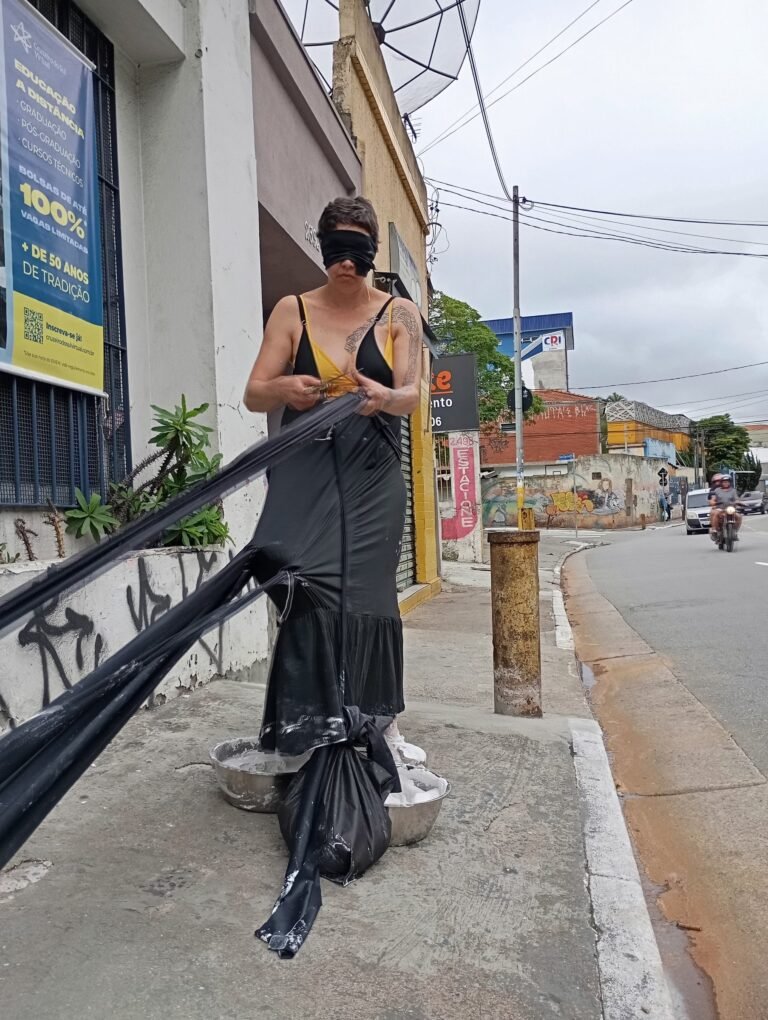 Kareen Labbé Weber, de vestido preto e óculos escuros, puxa longas tiras de tecido preto na calçada