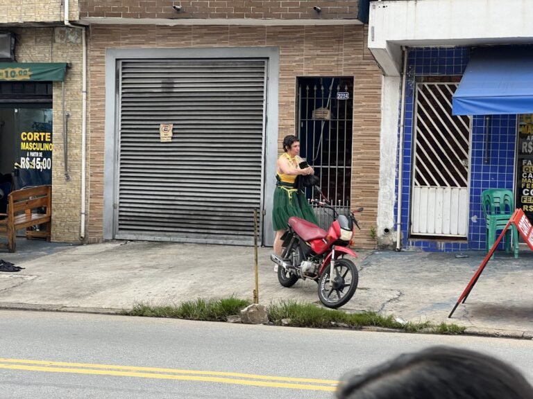 Kareen Labbé Weber caminha de saia verde por uma rua de Heliópolis, diante de portas de comércio