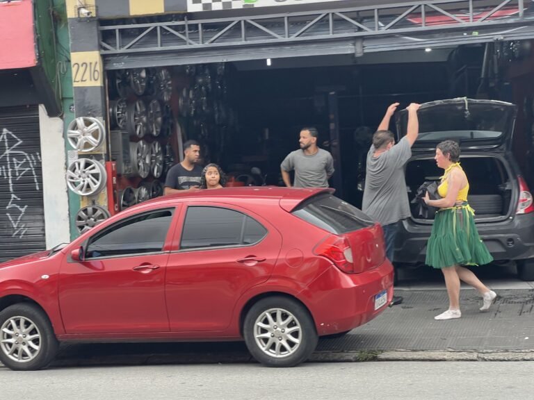 Kareen Labbé Weber carrega tecidos pretos diante de uma borracharia, entre carros e moradores