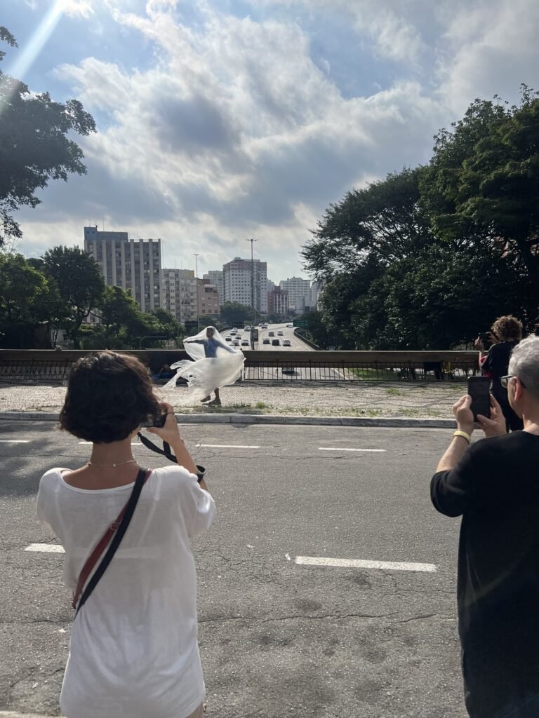 Público fotografa Thales Ferreira, que dança com o plástico junto à mureta, com a avenida ao fundo