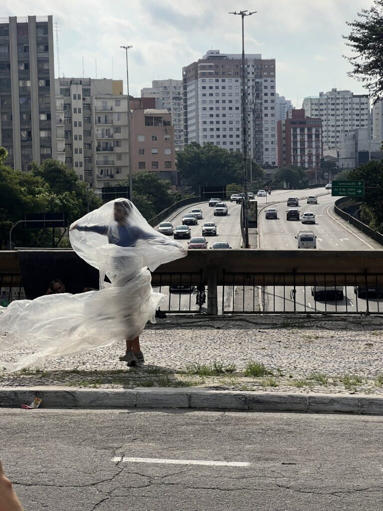 Thales Ferreira com a película plástica aberta pelo vento, diante da avenida e dos prédios