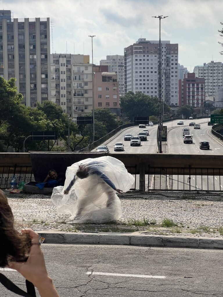 Thales Ferreira curvado sob o plástico inflado pelo vento, diante da avenida
