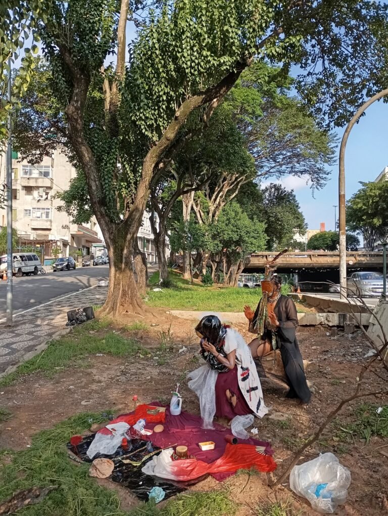 Integrantes do Triste Midríase montam um altar sobre tecido vermelho no terreno arborizado