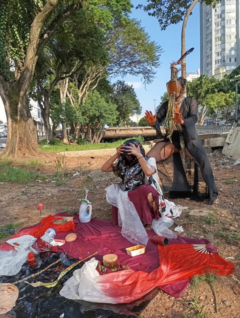 Integrante do Triste Midríase de rosto coberto sentado diante do altar, com a dupla de pé ao lado