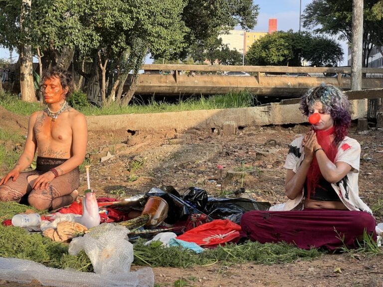 A dupla Triste Midríase sentada diante do altar, uma das pessoas de nariz de palhaço vermelho