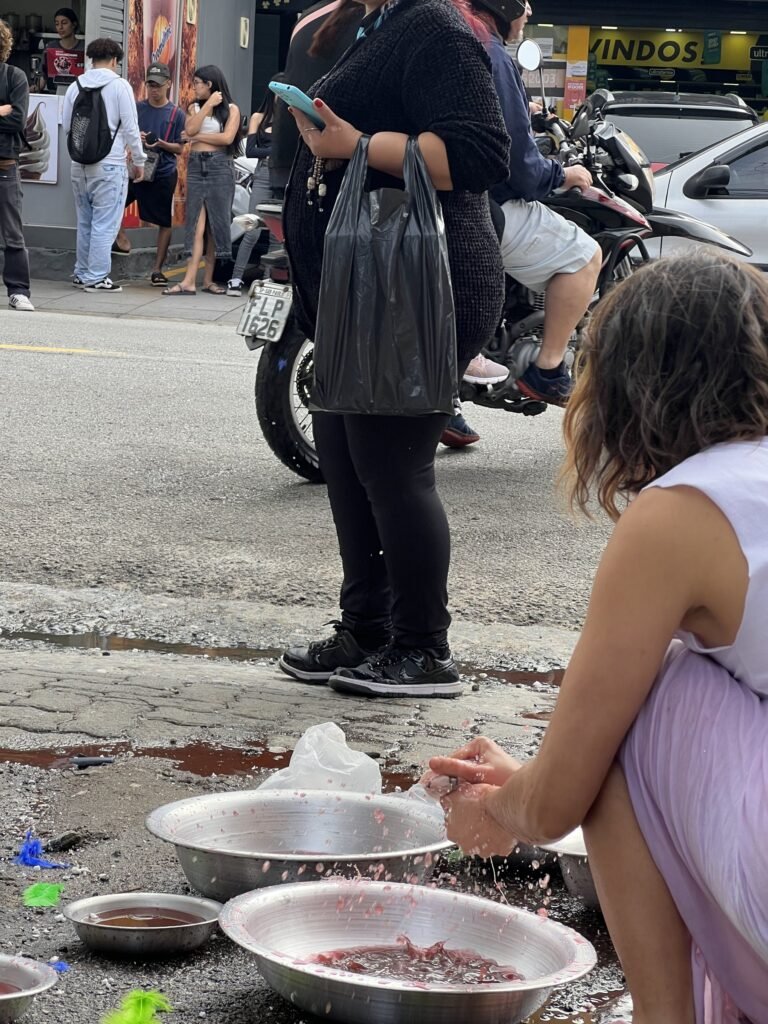Williana Silva agachada junto às bacias, com passantes na calçada