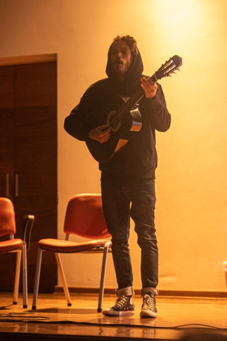 IsTo canta tocando violão no palco do auditório da Pinacoteca