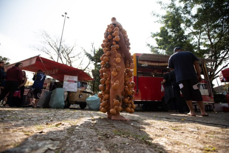 Jéssica Cruz, coberta de cabaças, parada no calçamento de pedra entre barracas e food trucks da feira