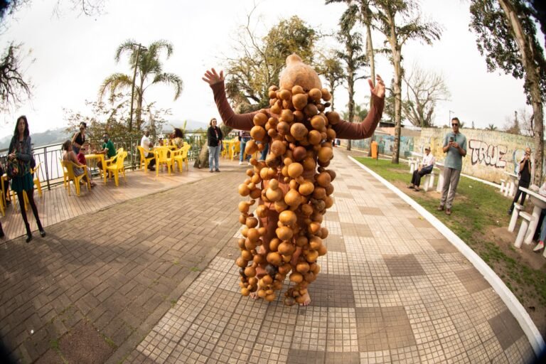 Jéssica Cruz abre os braços sob as cabaças no calçadão à beira da Represa Billings, com mesas e público ao redor