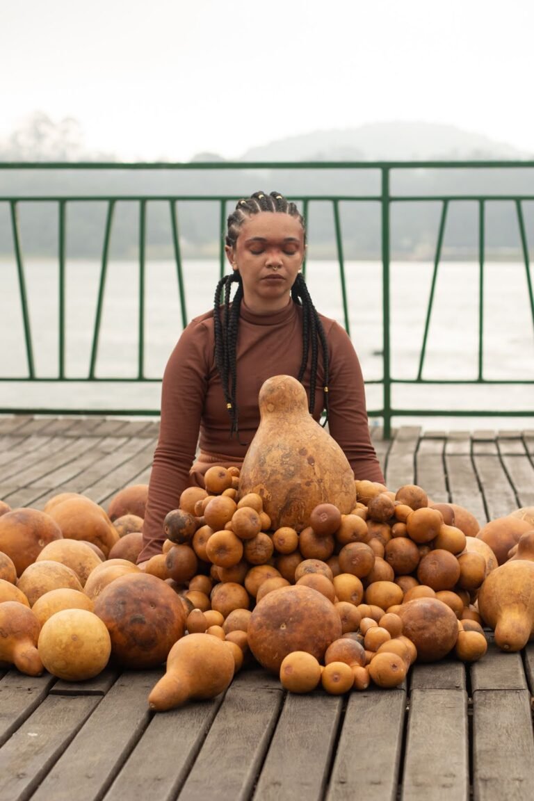 Jéssica Cruz, já sem o manto, sentada atrás do monte de cabaças no deck, de olhos fechados