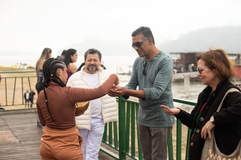 Jéssica Cruz entrega sementes nas mãos de pessoas do público no deck à beira da represa