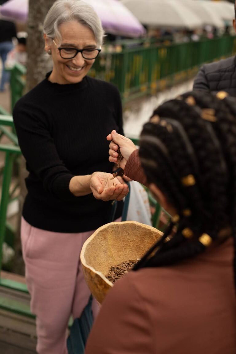 Uma mulher de cabelos grisalhos recebe sementes de Jéssica Cruz, que segura a cuia