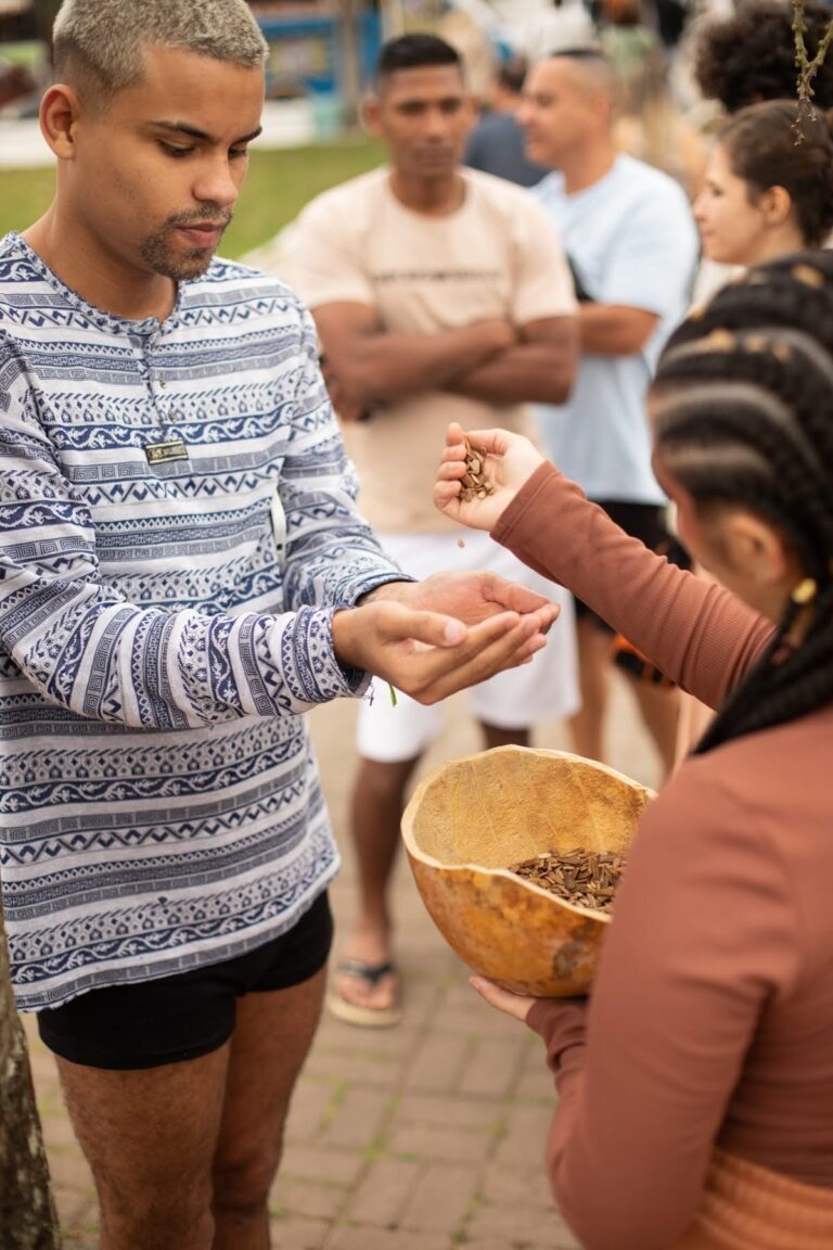 Um jovem recebe sementes nas mãos em concha, oferecidas por Jéssica Cruz com a cuia