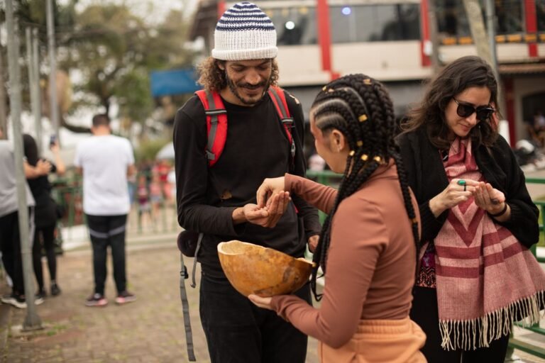 Jéssica Cruz oferece sementes da cuia a um homem de gorro listrado e a uma mulher de óculos escuros