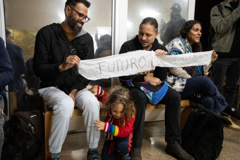 Um homem sentado entre o público segura a tira de pano com a palavra "futuro", com uma criança à frente