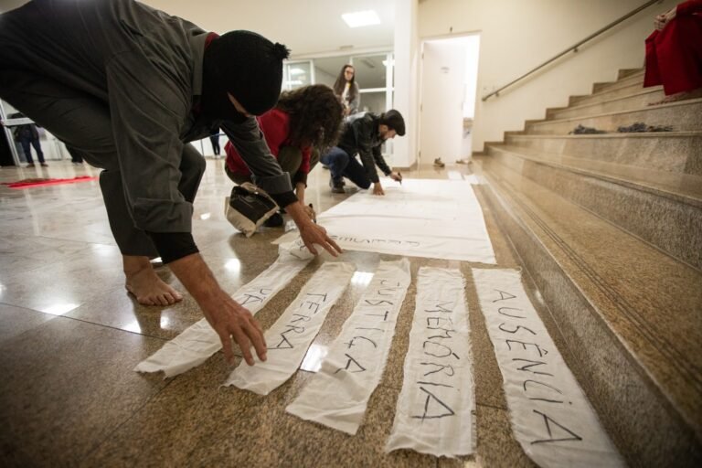 O performer encapuzado alinha ao pé da escadaria tiras de pano com as palavras "terra", "justiça", "memória" e "ausência"