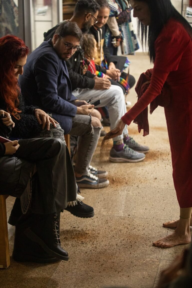 A performer de vermelho espalha terra junto aos pés do público sentado