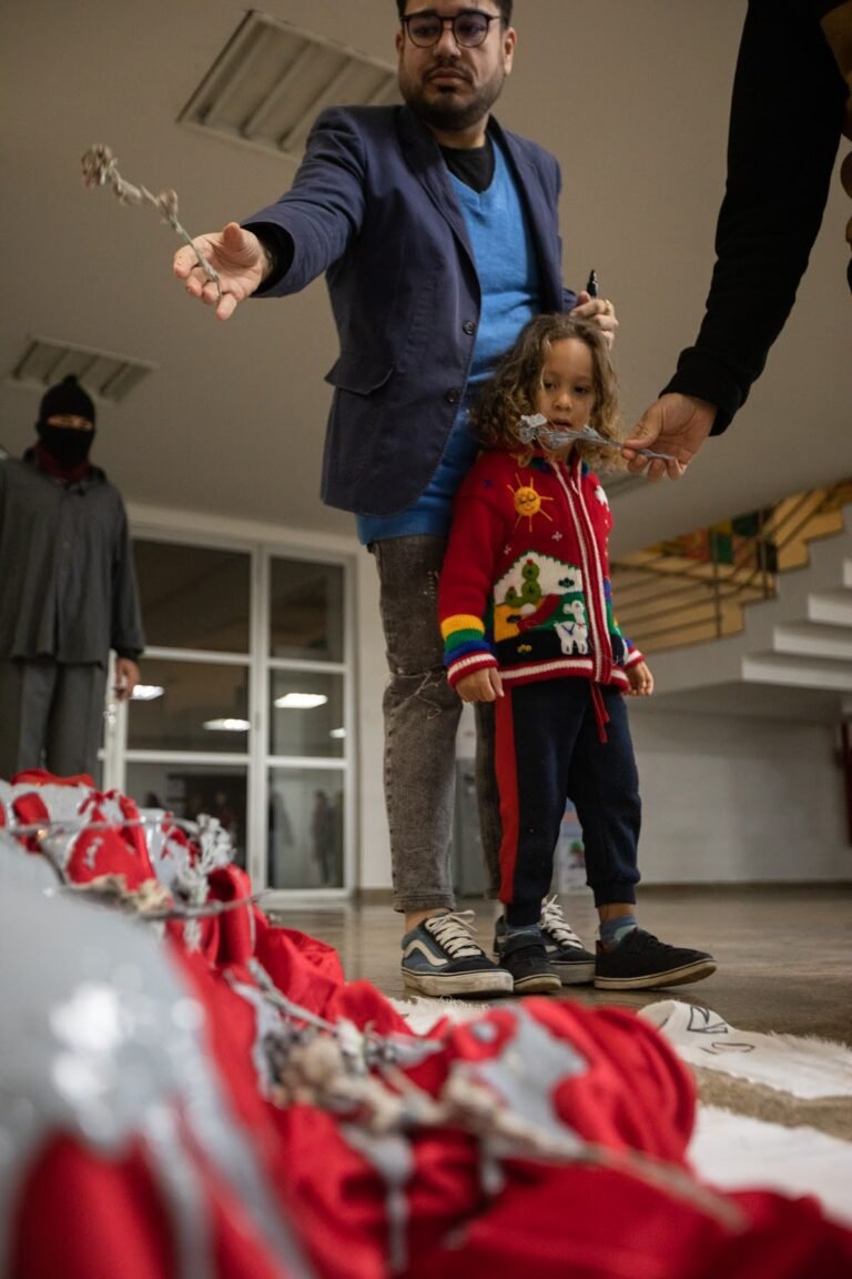 Um homem e uma criança lançam flores secas sobre o corpo envolto em vermelho e cinza