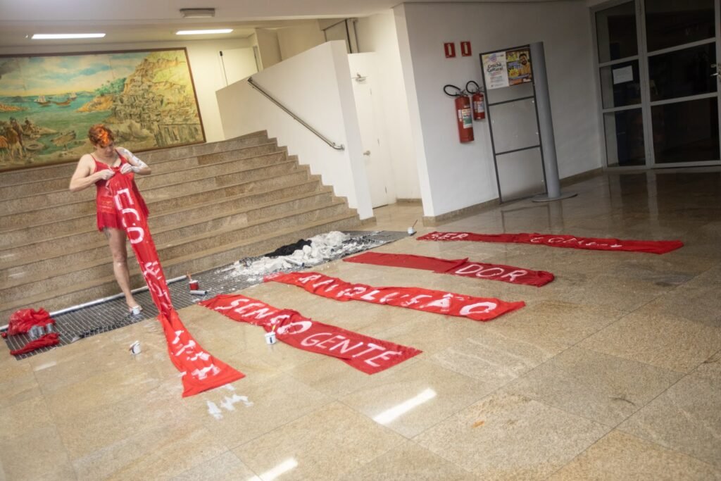 Kareen Labbé Weber, de vestido vermelho, segura uma faixa diante das faixas pintadas com palavras como "dor", "revolução" e "ser gente"