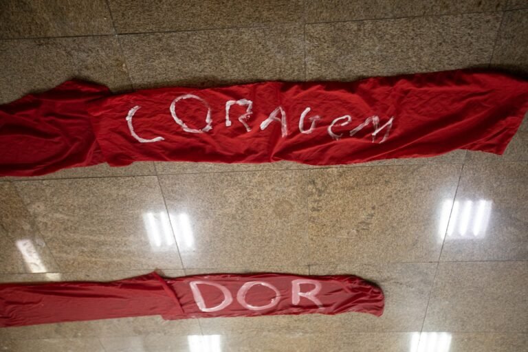 Faixas vermelhas no chão com as palavras "coragem" e "dor" pintadas em branco