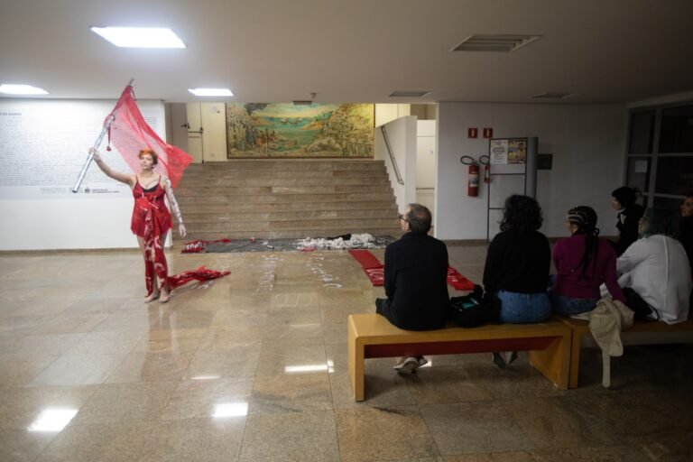 Kareen Labbé Weber ergue uma bandeira vermelha no saguão, diante do público sentado num banco