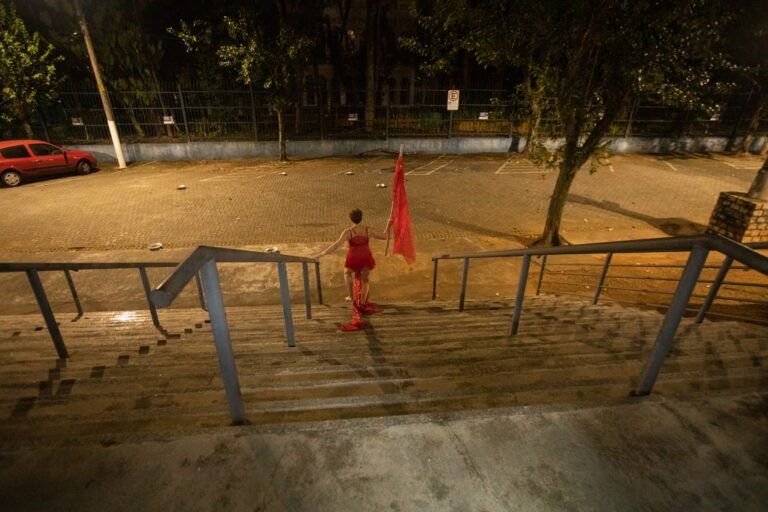 Kareen Labbé Weber desce sozinha a escadaria externa da Pinacoteca, à noite, levando a bandeira vermelha